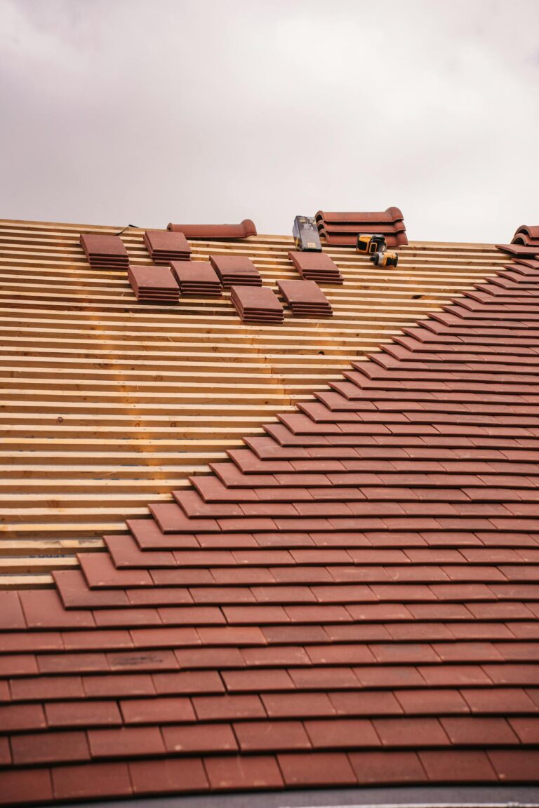 Partial installation of a terracotta tile roof on a building in progress.